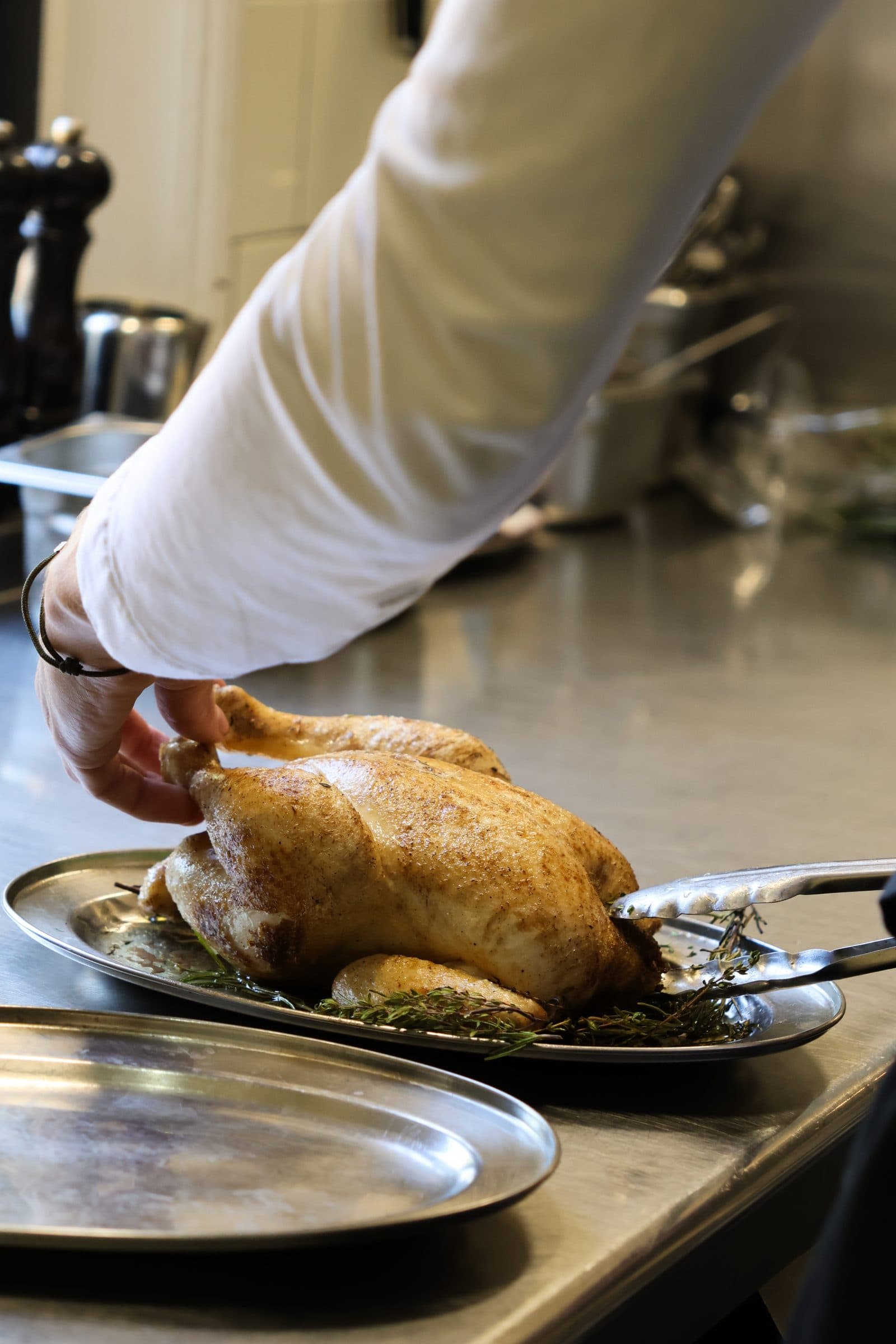 Kok tilt een goudbruin gebraden gevogelte met verse tijm van een schaal in de keuken.